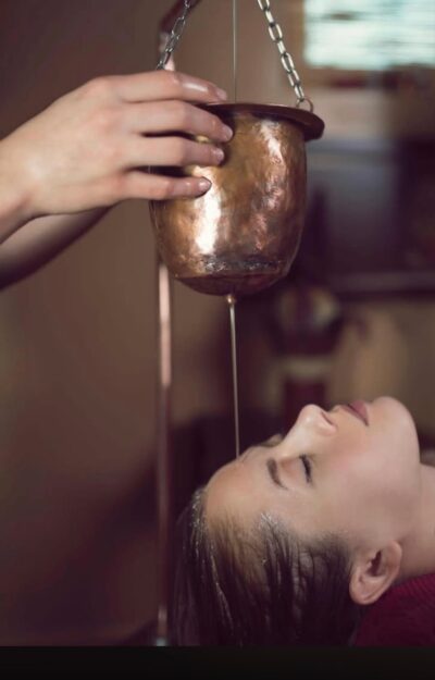 Warm oil streaming gently over the forehead of a woman receiving Shirodhara massage